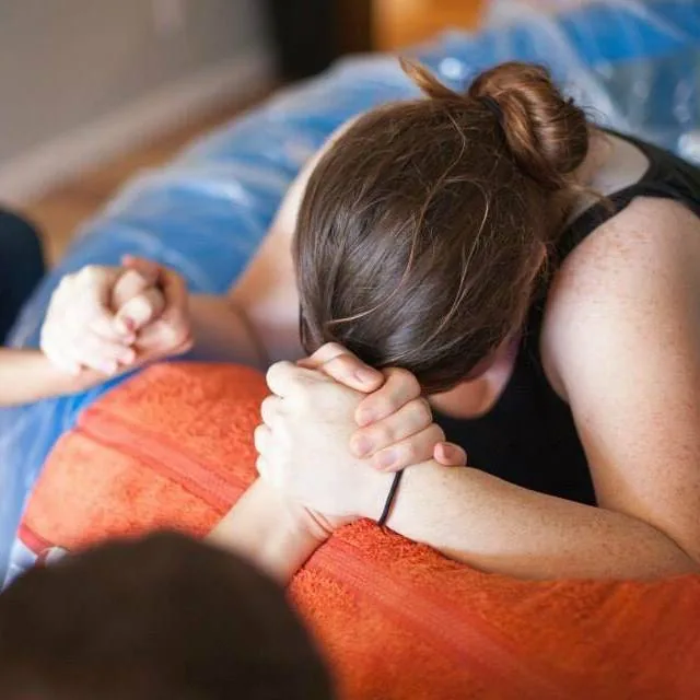 A mother leaning forward in labor while holding a support person’s hands